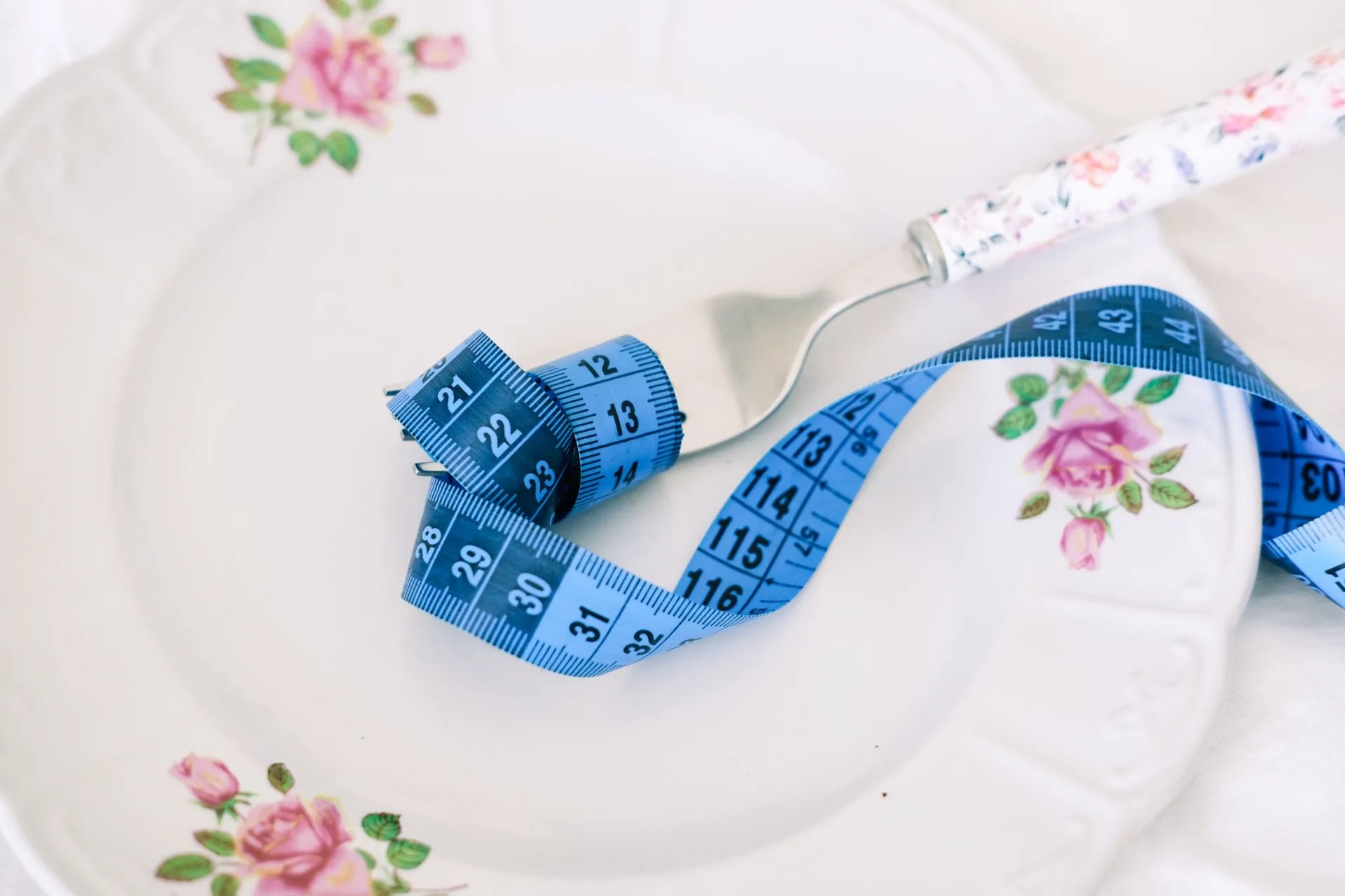 Bord met bloemmotief, vork en blauw meetlint als symbool voor gezond eten.