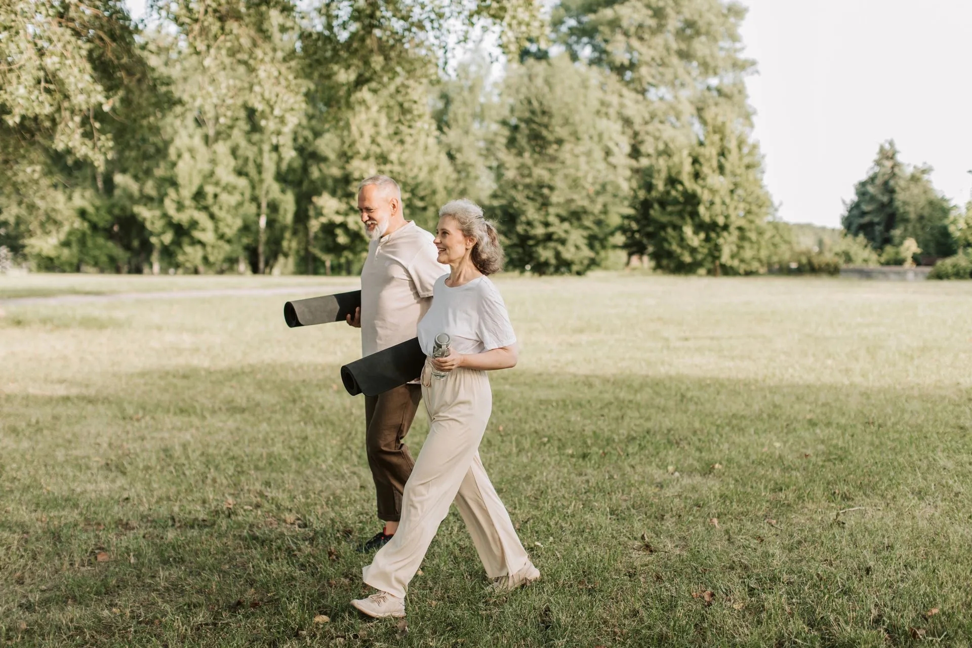 Ouder stel loopt met yogamatten over het gras op een zonnige dag.